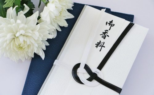 「御香料」と書かれた香典袋と白い菊の花が2輪ある写真